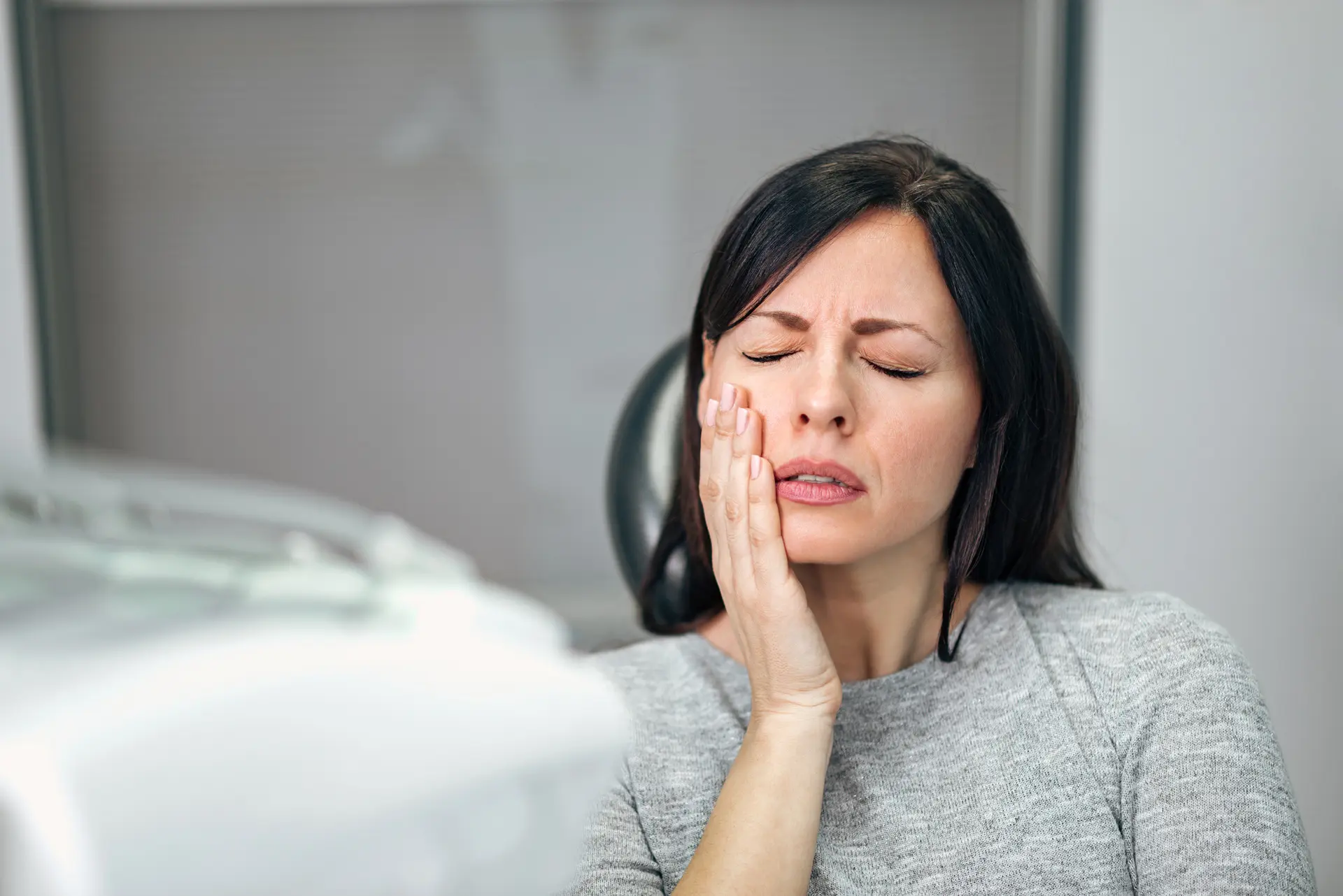 Woman holding jaw in pain while sitting in dental chair with toothache