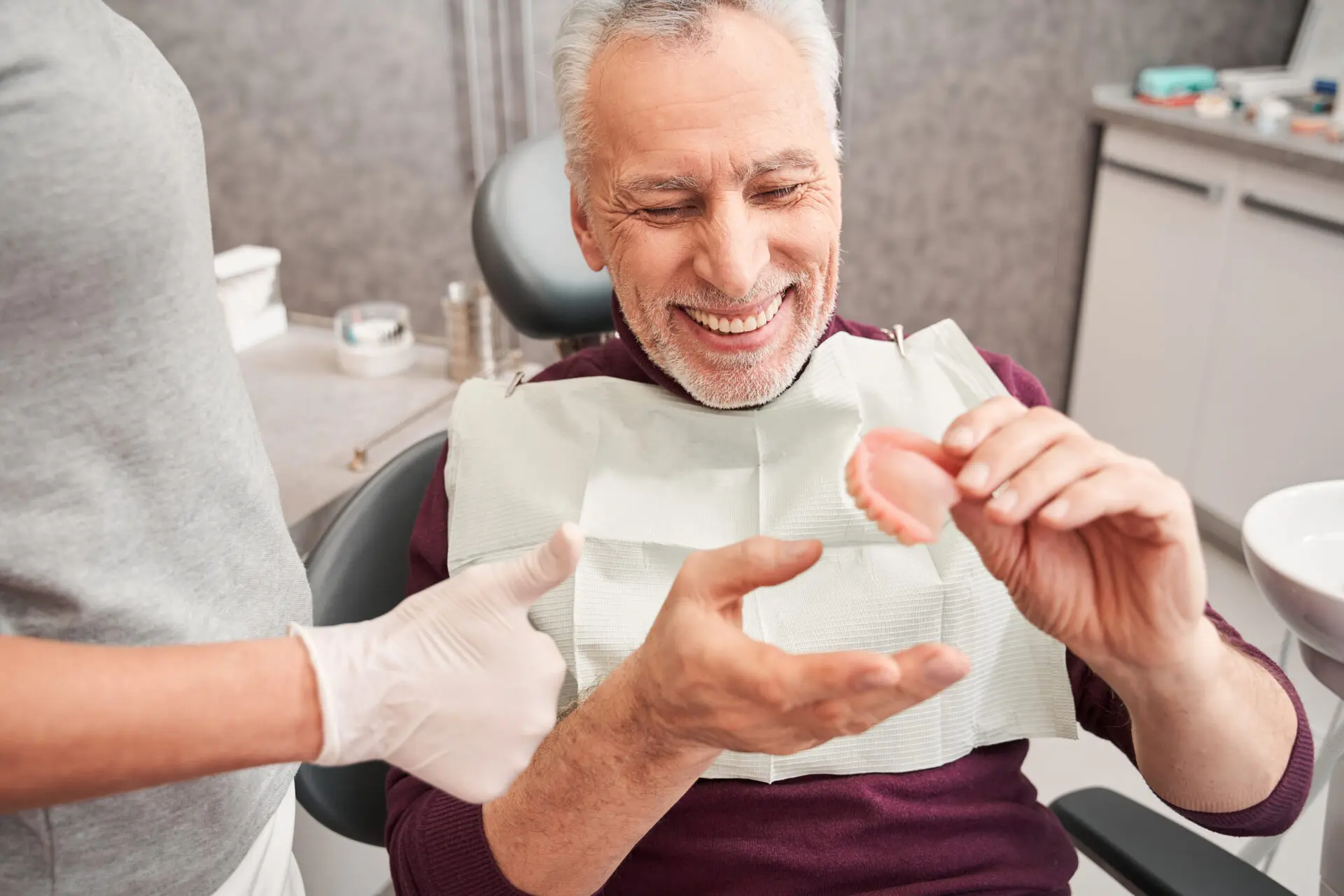 Smiling patient holding modern dentures during a consultation at an Ottawa dental clinic focused on natural-looking results