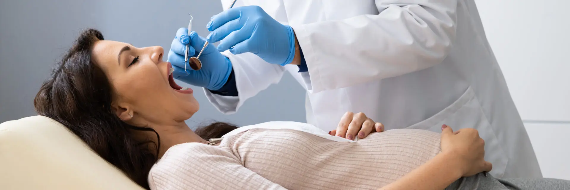Dentist treating the teeth of a pregnant woman lying in a dental chair during checkup.