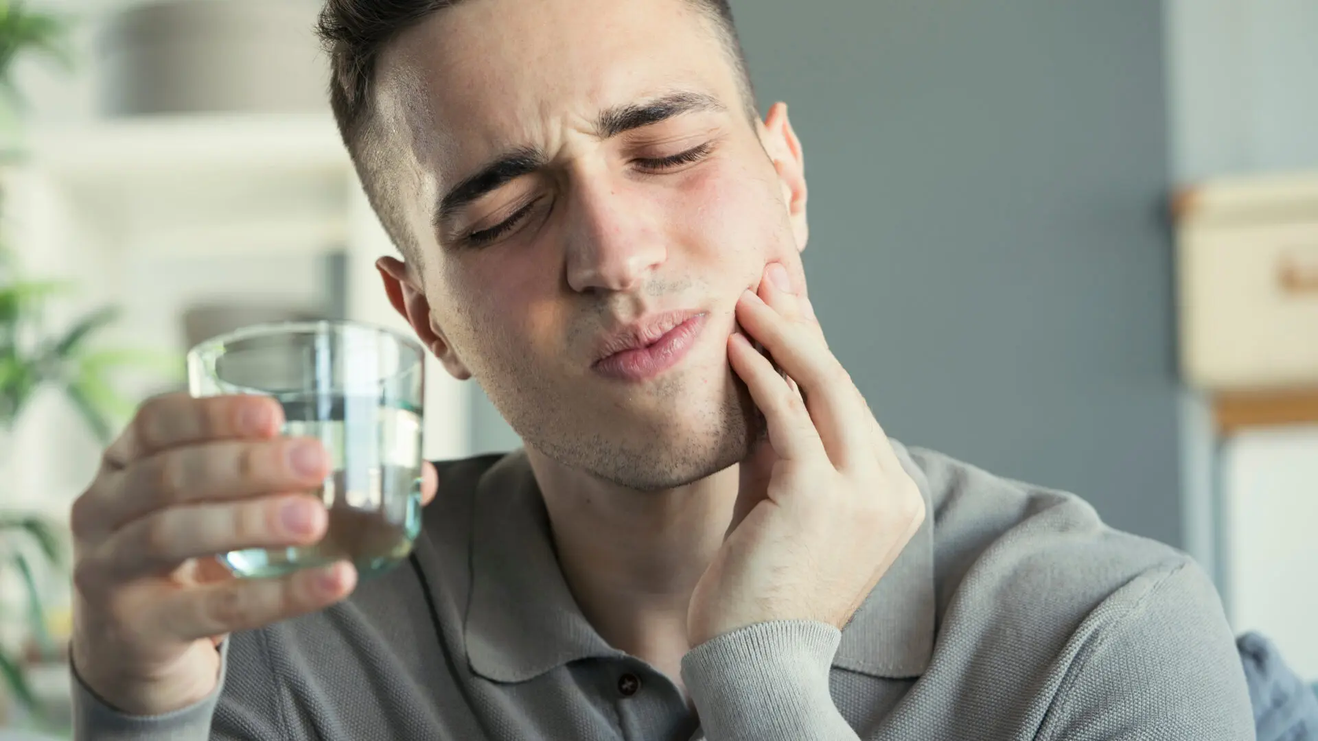 Man holding a glass of water while touching his cheek due to tooth sensitivity