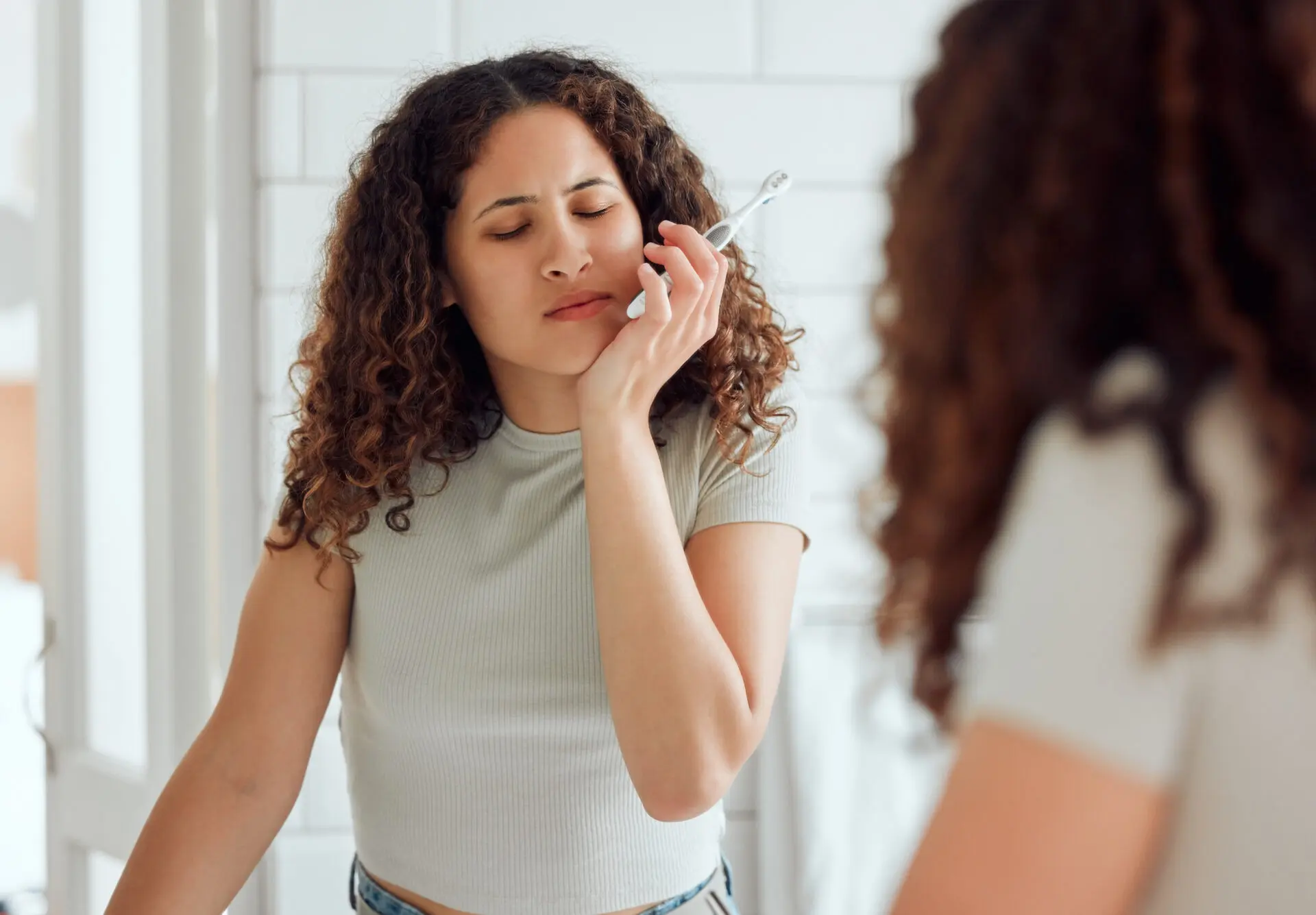 Woman holding a toothbrush and touching her cheek due to tooth pain