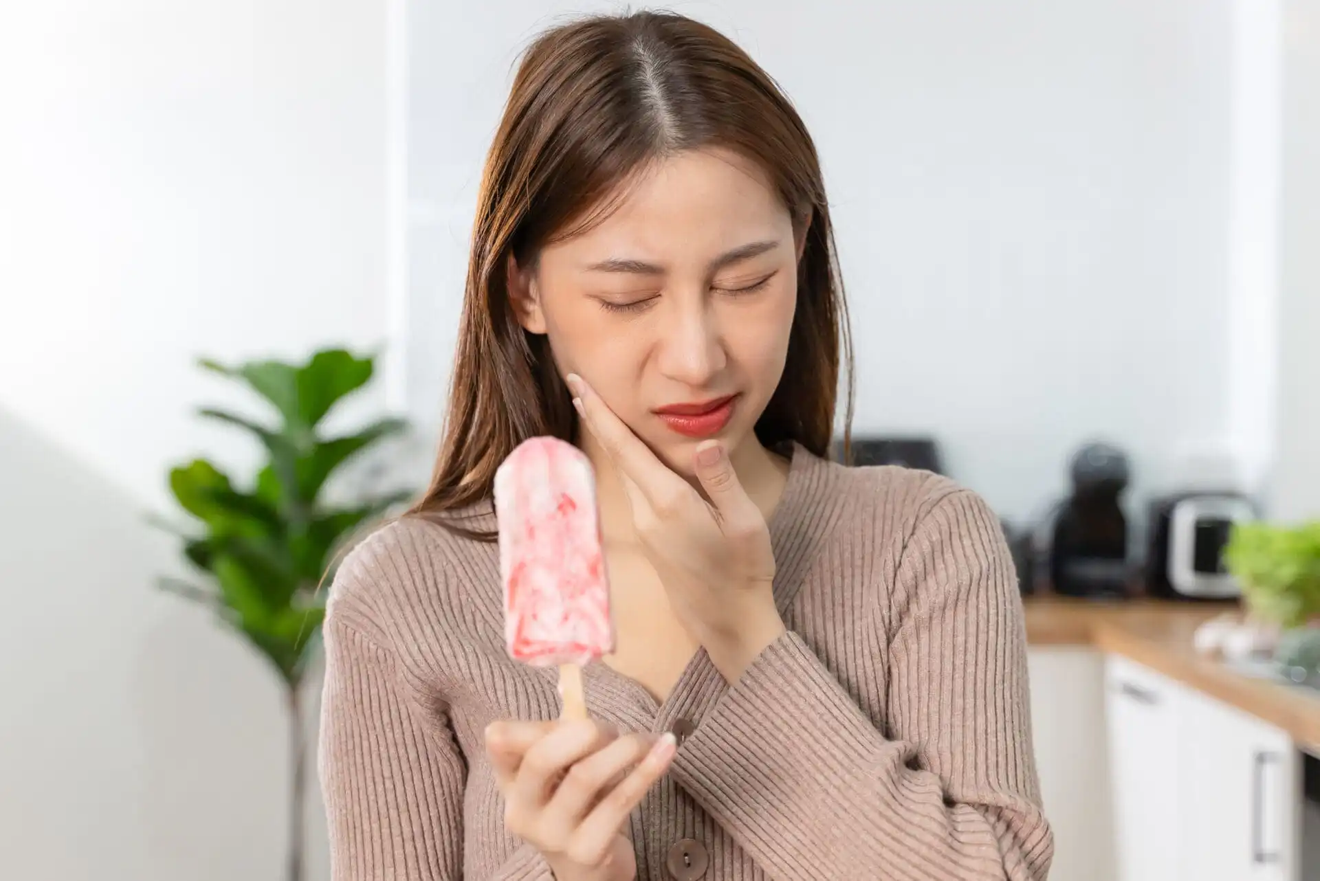 Asian Woman touching her chin feeling sensitive teeth when eating an ice cream. Have a gum and oral problem.