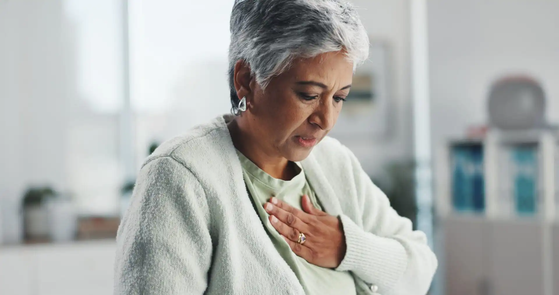 Senior woman with chest pain and heartburn at hospital checkup, showing symptoms of acid reflux or digestive discomfort.
