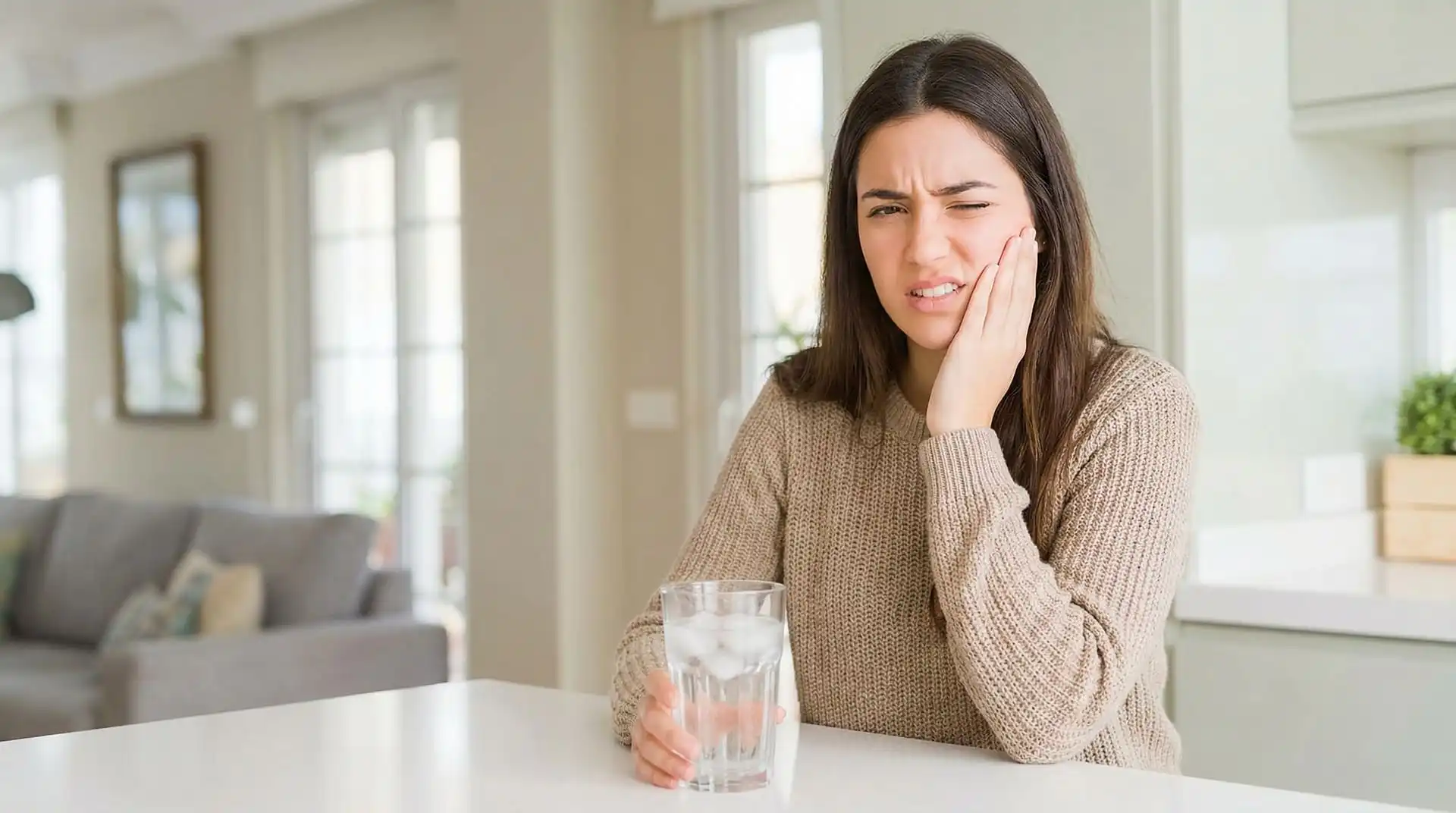Woman reacting to tooth pain while holding a glass of cold water, representing tooth sensitivity to hot and cold