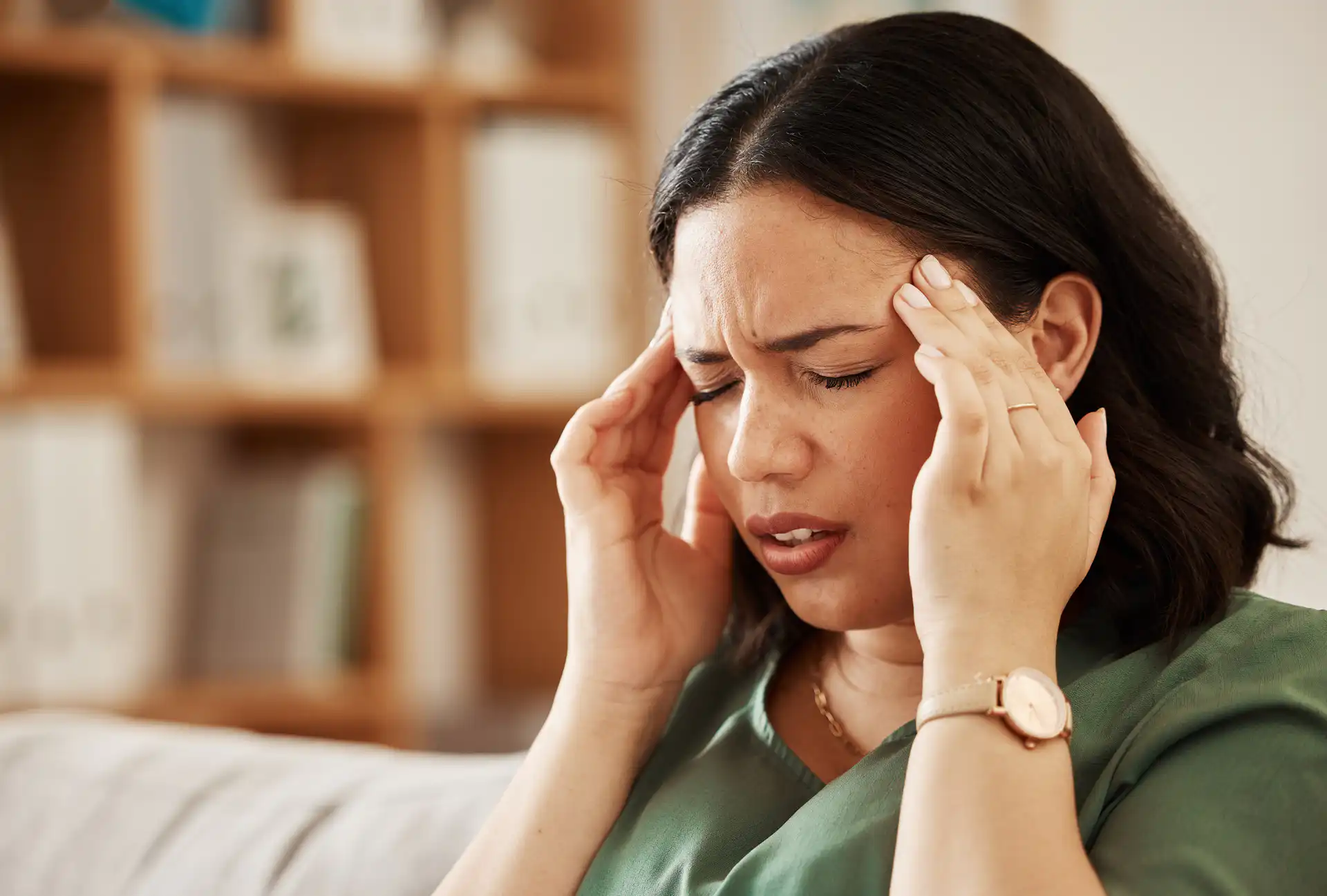 Woman holding both temples while experiencing a headache at home